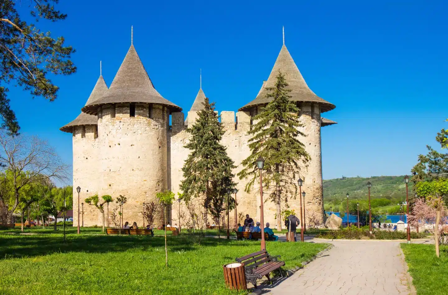 Soroca Fortress in Moldova with round stone towers, green park surroundings, and visitors in front of the historic walls.