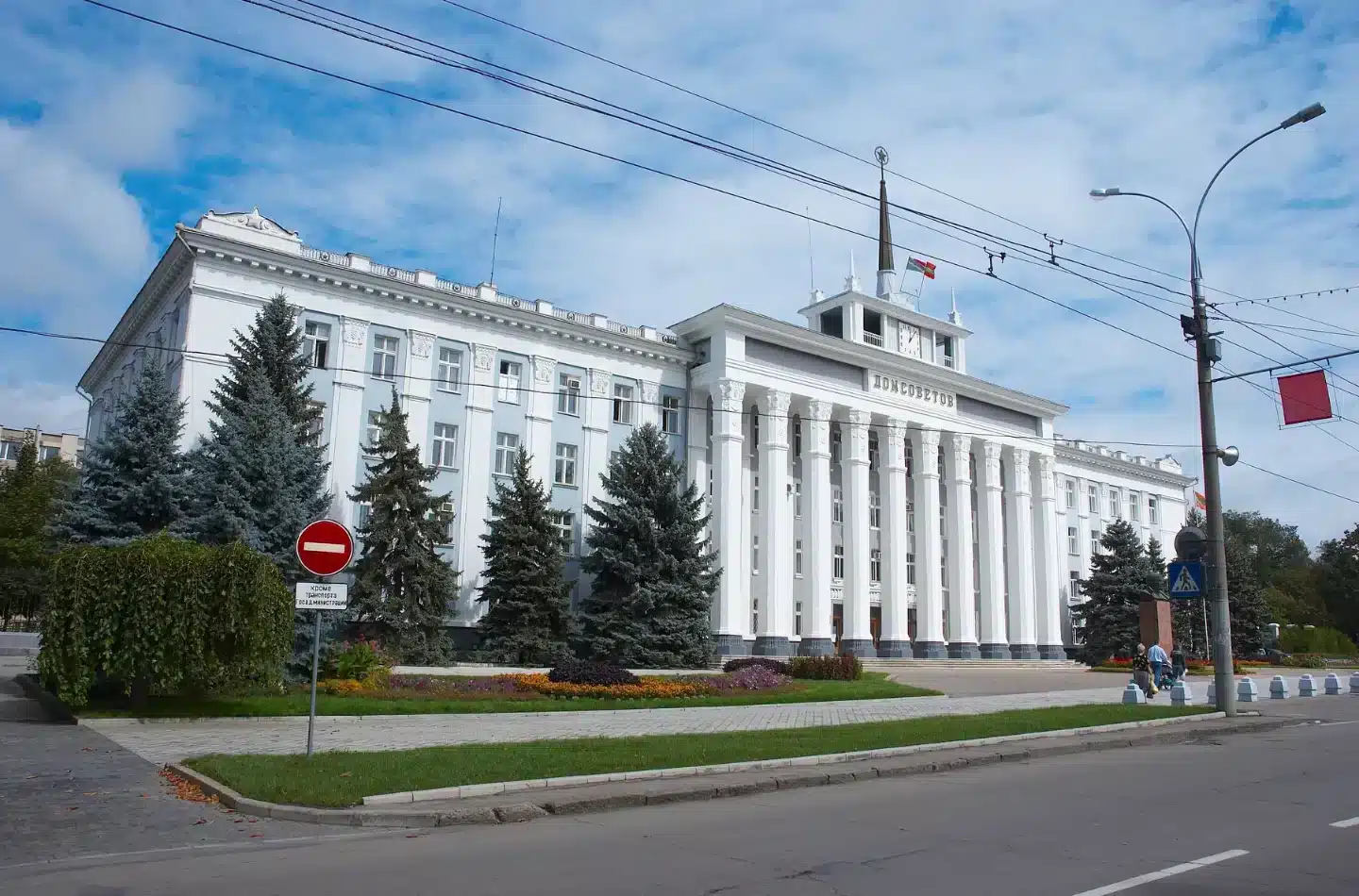 Tiraspol City Hall, a white administrative building with tall columns, flags, and evergreen trees along a wide boulevard.