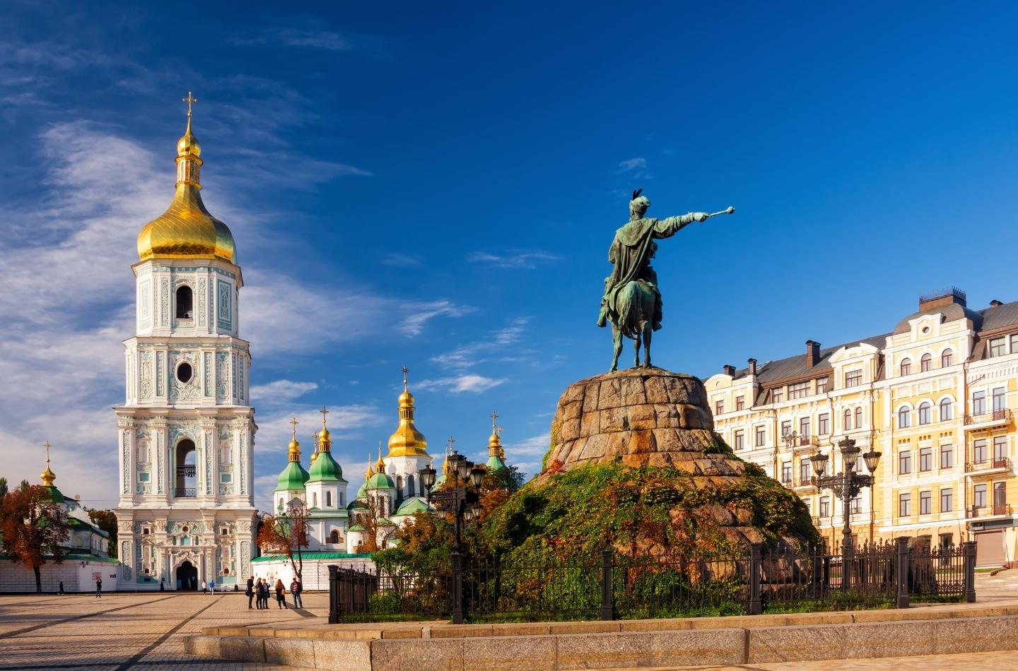 Equestrian statue of Bohdan Khmelnytsky on Sofiivska Square in Kyiv with the bell tower and golden domes of Saint Sophia Cathedral under a blue sky.